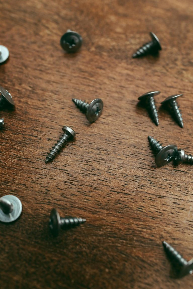 Close-up of scattered silver screws on a textured wooden surface, ideal for DIY and construction themes.